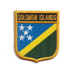 May include: Embroidered patch with the text "SOLOMON ISLANDS" in gold. The shield-shaped patch features a blue upper section with five white stars, a yellow diagonal stripe, and a green lower section.