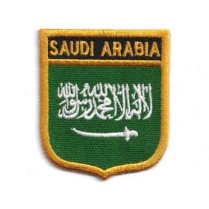 Puede incluir: Parche bordado con la bandera de Arabia Saudita. El parche tiene un fondo verde con escritura árabe blanca y una espada. Las palabras "SAUDI ARABIA" están bordadas en negro sobre un borde dorado.