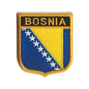 Può includere: Toppa ricamata raffigurante la bandiera della Bosnia ed Erzegovina. La toppa ha la forma di uno scudo con un bordo dorato. Il design della bandiera include un triangolo blu con stelle bianche, un campo giallo e la scritta "BOSNIA" in oro.