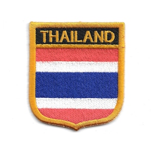 Puede incluir: Parche bordado con la bandera de Tailandia. El parche tiene forma de escudo con un borde dorado. El diseño de la bandera incluye franjas horizontales rojas, blancas y azules, con la palabra "THAILAND" en letras doradas en la parte superior.