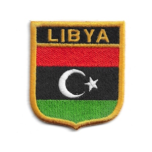 May include: Embroidered Libya flag patch with a gold border. The shield-shaped patch displays the flag's design: red, black, and green stripes, with a white crescent and star emblem in the centre. The word 'LIBYA' is embroidered at the top.