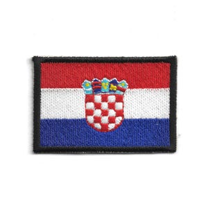 Może przedstawiać: Haftowana naszywka z flagą Chorwacji. Projekt zawiera czerwone, białe i niebieskie poziome paski z chorwackim herbem pośrodku. Naszywka ma czarną obwódkę.