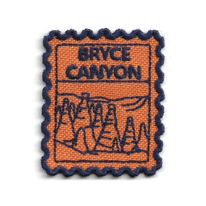 May include: A rectangular embroidered patch with a scalloped dark blue border. The background is orange fabric. The text BRYCE CANYON is stitched in dark blue at the top. Below the text is a dark blue line drawing of rock formations and hoodoos.