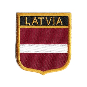 May include: Embroidered patch featuring the flag of Latvia. The patch has a shield shape with a gold border. The flag design includes a maroon background with a white stripe and the word "LATVIA" in gold letters.