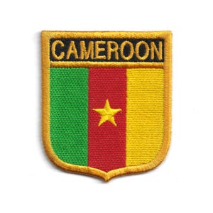 May include: Embroidered patch in the shape of a shield, featuring the flag of Cameroon. The patch has a gold border and the word "CAMEROON" in black letters at the top. The flag design includes green, red, and yellow vertical stripes, with a yellow star in the center.