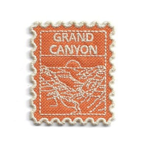 May include: Embroidered patch featuring the words "GRAND CANYON" above a landscape design. The patch has a textured orange background with white stitching and a scalloped border. Ideal for jackets, bags, or other fabric items.