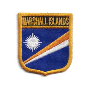 May include: Embroidered patch featuring the Marshall Islands flag design. The patch has a blue background with a white sun and a diagonal orange and white stripe. The text "MARSHALL ISLANDS" is embroidered in gold.