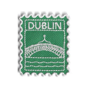 以下が含まれることがあります： 緑色の生地パッチ。白い刺繍で橋のデザインと「DUBLIN」の文字が施されています。パッチは切手のようなスカラップエッジです。橋のデザインはアーチと線で詳細に描かれています。