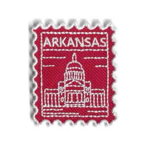 May include: A red fabric patch with a white embroidered design of the Arkansas State Capitol building. The word "ARKANSAS" is embroidered at the top. The patch has a postage stamp-like border.