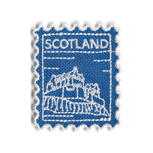 Op de afbeelding: Een blauwe stoffen patch in de vorm van een postzegel. Het woord "SCOTLAND" is in het wit geborduurd aan de bovenkant. Een wit geborduurd beeld van een bergketen en een structuur staat in het midden. De randen zijn geschulpt met witte draad.