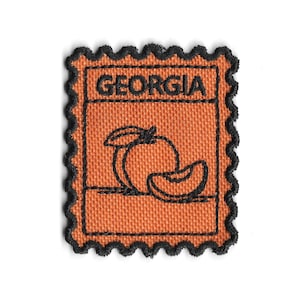 Peut inclure: Écusson en tissu orange avec une bordure festonnée noire. Le patch comporte le mot "GEORGIA" en lettres noires en bloc au-dessus d'un dessin au trait noir d'une pêche et d'une tranche de pêche.