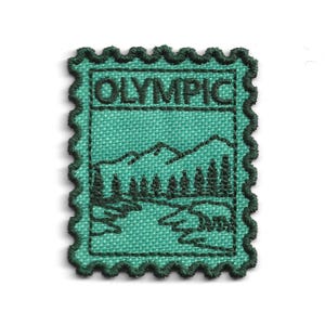 Op de afbeelding: Een rechthoekige geborduurde patch met een geschulpte rand, voorzien van een groenblauwe achtergrond en donkergroen stiksel. Het ontwerp toont een berglandschap met bomen en een rivier, met het woord OLYMPIC in donkergroen bovenaan geborduurd.