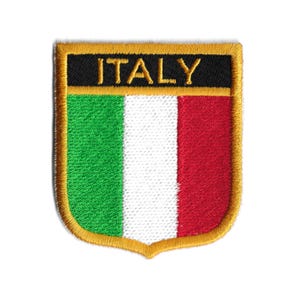 Può includere: Una toppa ricamata con i colori della bandiera italiana: verde, bianco e rosso. La toppa è circondata da un bordo dorato e ha la scritta "ITALIA" in lettere nere nella parte superiore.