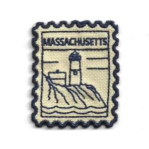 May include: A rectangular embroidered patch with a scalloped edge, featuring a cream-coloured fabric base and dark blue stitching. The design depicts a lighthouse on a rocky coastline with the word MASSACHUSETTS embroidered in dark blue text.