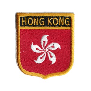 May include: Embroidered patch featuring the Hong Kong flag design. The patch has a red background with a white Bauhinia flower and the words "HONG KONG" in black letters. The patch is bordered with gold stitching.