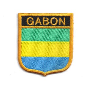 May include: Embroidered patch with the word "GABON" in gold on a black panel. The shield-shaped patch displays green, yellow, and blue horizontal stripes, with a gold border.