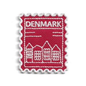 Peut inclure: Un écusson brodé rectangulaire à bord festonné, présentant un fond rouge profond et des coutures blanches. Le motif représente une rangée de quatre maisons aux toits en pignon et le mot DENMARK brodé en blanc au centre supérieur.