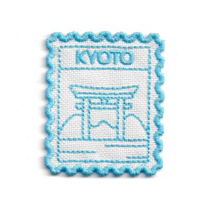 Peut inclure: Écusson brodé avec un bord festonné bleu clair. Le mot "KYOTO" est brodé en haut. En dessous, une image brodée en bleu clair d'un torii japonais et de montagnes, ressemblant à un timbre-poste.