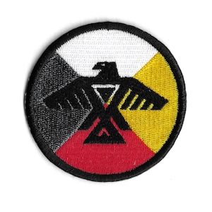 Może przedstawiać: Okrągła, haftowana naszywka z czarnym orłem pośrodku. Koło podzielone jest na cztery sekcje: białą, żółtą, czerwoną i czarną. Naszywka ma czarną obwódkę.