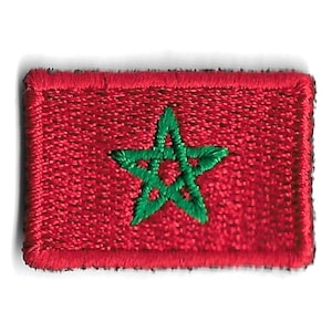 Puede incluir: Un parche rojo bordado con una estrella verde de cinco puntas en el centro. La estrella tiene un diseño único con múltiples puntos.