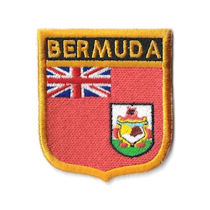 May include: A gold embroidered patch featuring the word "BERMUDA" in black lettering and the Bermuda flag. The flag displays a red field with a Union Jack in the top left corner and the Bermuda coat of arms in the bottom right corner.