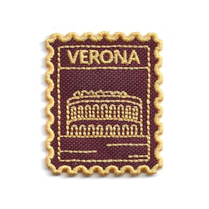 Può includere: Una toppa ricamata rettangolare con bordo smerlato, caratterizzata da uno sfondo bordeaux scuro e dettagli in filo dorato. Il design raffigura una struttura architettonica con la parola VERONA ricamata in oro nella parte superiore.