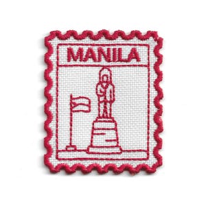 May include: Embroidered patch in the shape of a postage stamp, with the word "MANILA" at the top. The design shows a statue on a pedestal and a flag, all in red thread on a white background. The patch has a scalloped red border.