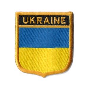 Könnte beinhalten: Ein gestickter Aufnäher in Gelb und Blau mit dem Wort "UKRAINE" in schwarzen Buchstaben.