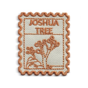 May include: Embroidered patch featuring a Joshua Tree design. The patch has a light beige background with a brown Joshua Tree illustration and text. The border is a scalloped brown edge, resembling a postage stamp.