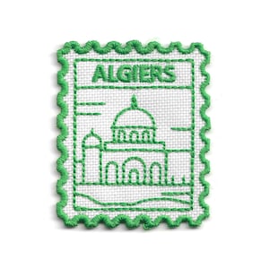 May include: Embroidered patch in the shape of a postage stamp, featuring the word "ALGIERS" and a green outline of a building with a dome. The patch has a white background and a green, scalloped border.
