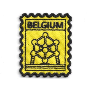 Könnte beinhalten: Ein rechteckiger gestickter Aufnäher mit gelbem Hintergrund und schwarzem Rand mit gezackten Kanten. Der Aufnäher zeigt das Wort BELGIUM in schwarzen Großbuchstaben über einer schwarzen Strichzeichnung des Atomium-Bauwerks in Brüssel.