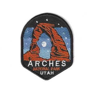 Puede incluir: Parche bordado con el icónico arco del Parque Nacional Arches en tonos naranja y marrón sobre un cielo azul estrellado. El parche incluye el texto "ARCHES NATIONAL PARK UTAH" en letras blancas con un borde negro.