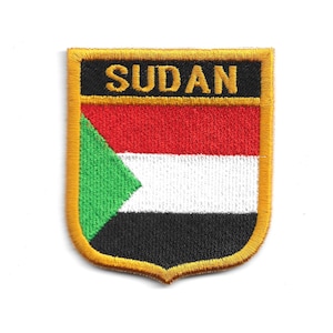 May include: Embroidered patch of the Sudanese flag. The patch is shield-shaped with a gold border. The flag design features red, white, and black horizontal stripes, with a green triangle on the left. The word "SUDAN" is embroidered in gold across the top.