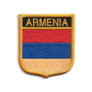 May include: Embroidered patch featuring the Armenian flag. The patch has a shield shape with a gold border. The flag design includes horizontal stripes of red, blue, and tan, with the word "ARMENIA" in black letters at the top.