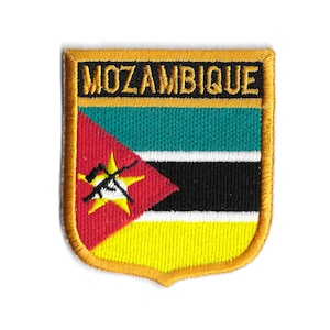 May include: An embroidered patch featuring the flag of Mozambique. The patch is shaped like a shield with a gold border and the word "MOZAMBIQUE" in gold lettering at the top. The flag is red, green, black, and yellow with a white star and a gun.