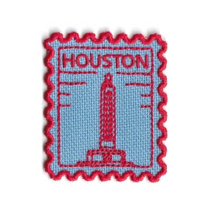 Peut inclure: Un écusson carré avec un fond bleu clair et une bordure rouge. L'écusson présente le mot "HOUSTON" en haut et une illustration rouge d'un grand bâtiment. L'écusson a une bordure rouge décorative et ondulée.