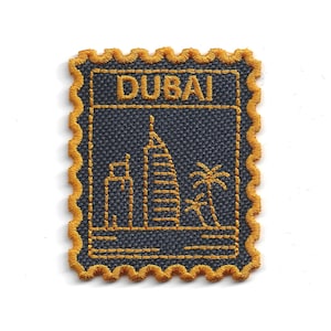 Op de afbeelding: Geborduurde patch met een gestileerd ontwerp van Dubai. De marineblauwe patch heeft een gouden rand en toont de skyline van de stad, inclusief het Burj Al Arab hotel en een palmboom. Het woord "DUBAI" is bovenaan geborduurd.