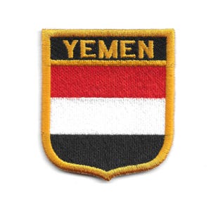 Puede incluir: Parche bordado con la bandera de Yemen. El parche en forma de escudo tiene un borde dorado y la palabra "YEMEN" en letras doradas. El diseño de la bandera presenta franjas horizontales rojas, blancas y negras.