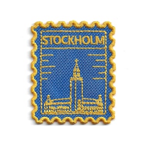May include: A blue embroidered patch with a yellow scalloped border. The patch features the word "STOCKHOLM" and a yellow illustration of a building. The rectangular patch is reminiscent of a postage stamp.