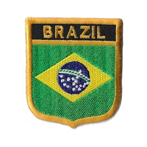 May include: Embroidered patch with the Brazilian flag in the center. The flag is green, yellow, and blue with a circle of white stars. The patch is surrounded by a gold border and the word "BRAZIL" is written in black letters at the top.
