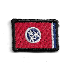 Könnte beinhalten: Ein gestickter Aufnäher mit der Staatsflagge von Tennessee. Die Flagge ist rot mit einem weißen Kreis, in dem sich drei weiße Sterne befinden, umgeben von einem blauen Ring. Der Aufnäher hat einen schwarzen Rand.