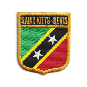 May include: Embroidered patch of the Saint Kitts-Nevis flag. The shield-shaped patch has a green upper left, red lower right, and black diagonal stripe with two white stars. The text "SAINT KITTS-NEVIS" is embroidered at the top.