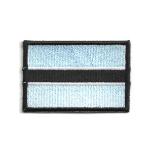May include: Embroidered patch depicting the flag of Botswana. The rectangular patch has a light blue background with a black stripe in the centre, bordered by a thin white stripe. The patch is outlined with a black border.
