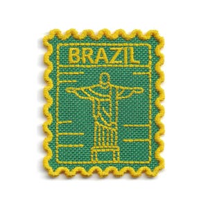 May include: A rectangular embroidered patch with a scalloped yellow border on a green fabric base. The design features the yellow stitched text BRAZIL above a yellow outline of the Christ the Redeemer statue with arms outstretched.