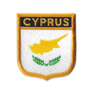 Könnte beinhalten: Ein gestickter Aufnäher mit weißem Hintergrund, gelber Umrandung und dem Wort "CYPRUS" in schwarzen Buchstaben. Der Aufnäher zeigt die Flagge von Zypern, die eine gelbe Karte der Insel auf weißem Hintergrund mit einem grünen Olivenzweig enthält.