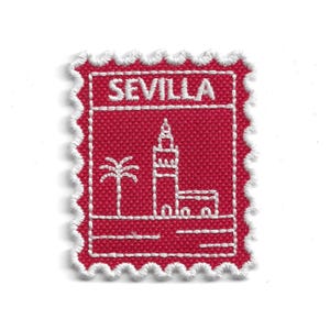 Può includere: Una toppa in tessuto rosso con dettagli ricamati bianchi. La toppa presenta la scritta "SEVILLA" in alto e un disegno di una palma e di un edificio. La toppa ha un bordo bianco smerlato.