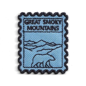 May include: A light blue patch with a black border and the text "GREAT SMOKY MOUNTAINS". The patch features a mountain range and a bear illustration. The patch has a postage stamp design.