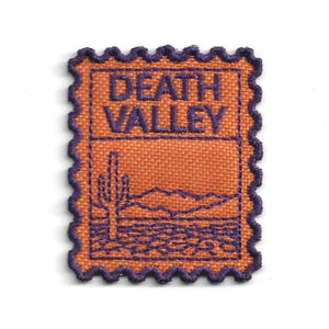 May include: A rectangular embroidered patch with a scalloped edge, featuring an orange background and purple stitching. The text DEATH VALLEY is embroidered at the top, with a desert landscape including a cactus and mountains below.