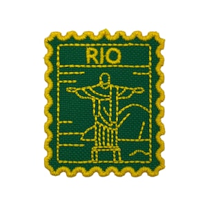 以下が含まれることがあります： 緑色の背景に黄色の縁取りとボーダーが施された刺繍パッチ。リオデジャネイロのキリスト像が描かれ、上部に「RIO」の文字。パッチは長方形で、スカラップエッジが付いています。