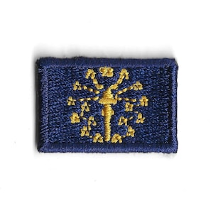 May include: A blue embroidered patch with a gold tree design. The tree has a single trunk and many branches with leaves. The patch is rectangular and has a white border.